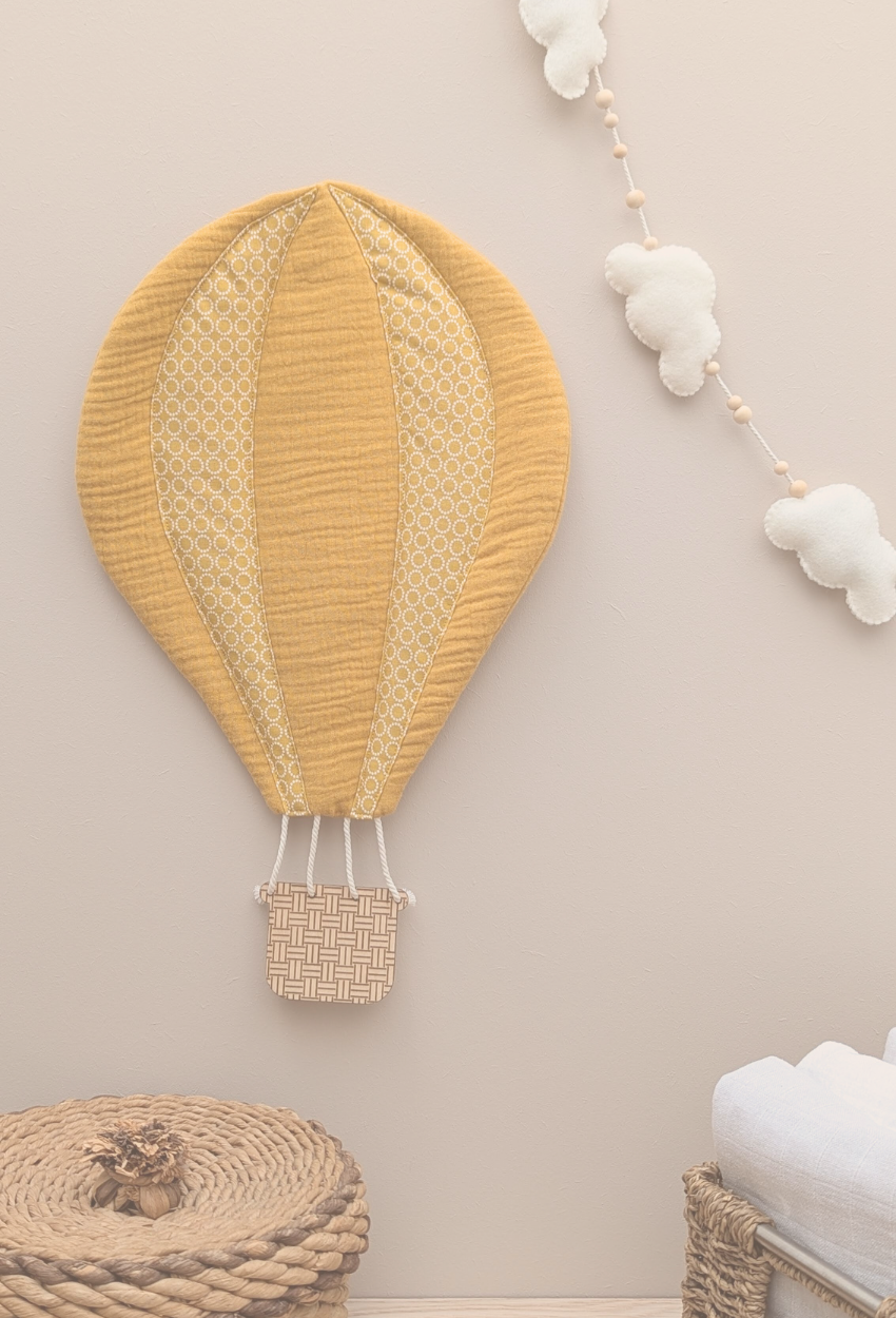 Décoration murale pour enfants en forme de montgolfière accrochée sur un mur dans une chambre avec des accessoires bébé.